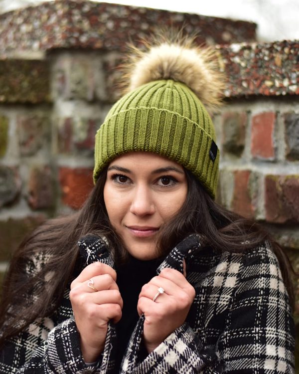 Woman wearing a green ribbed knit beanie with fur pom